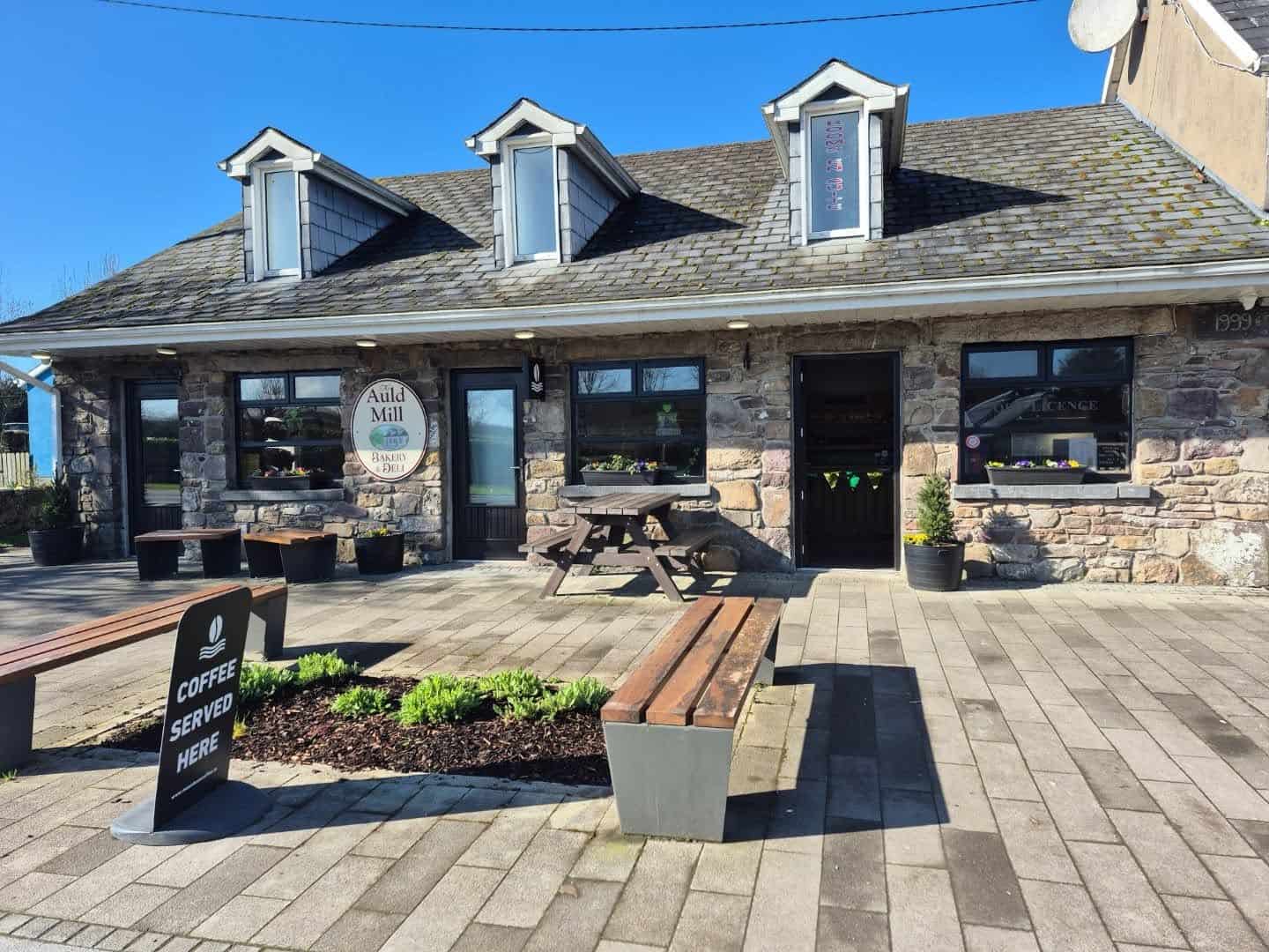 Auld Mill Bakery exterior with outdoor seating and a welcoming sign.