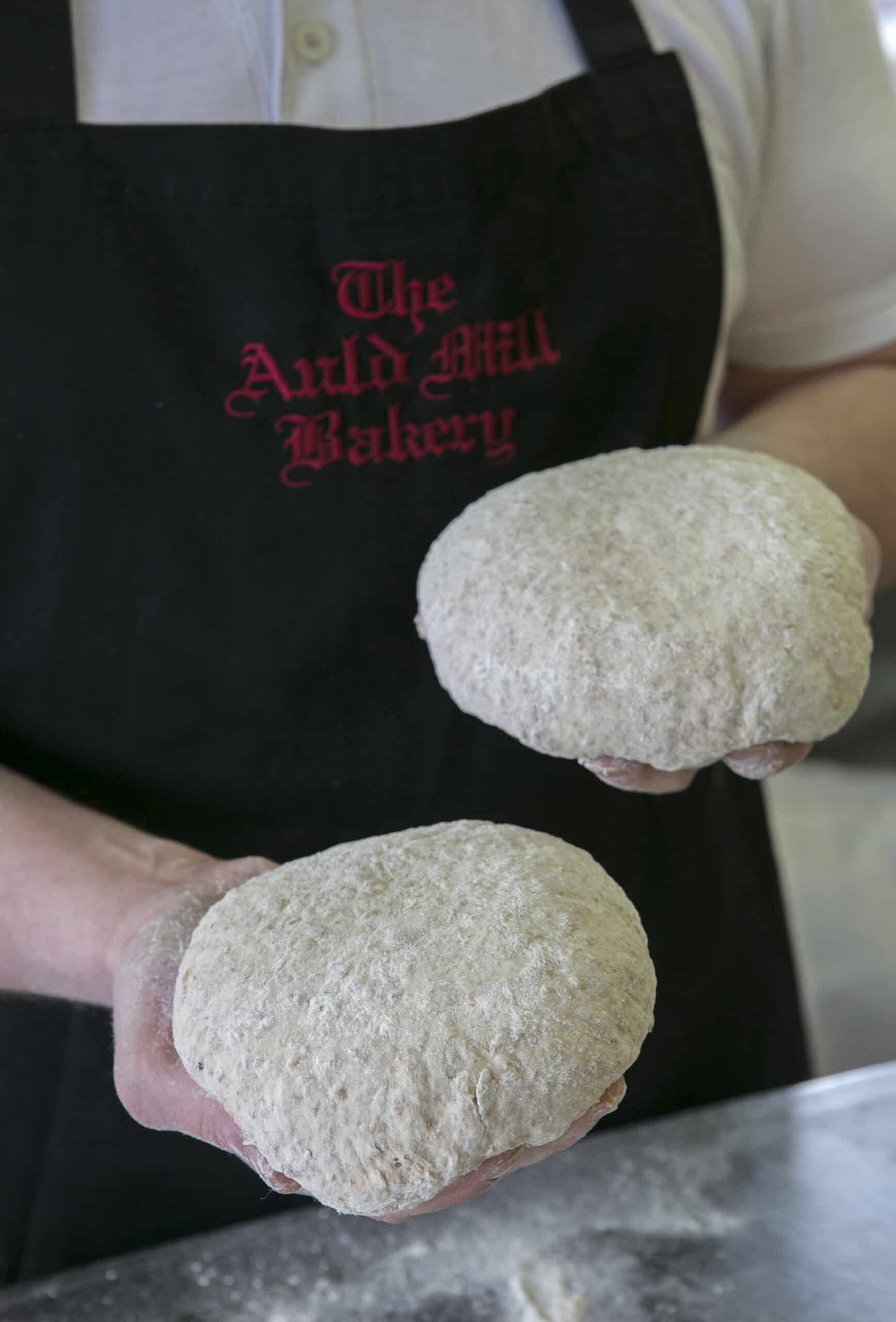 Freshly baked bread loaves held by a baker at The Auld Mill Bakery.