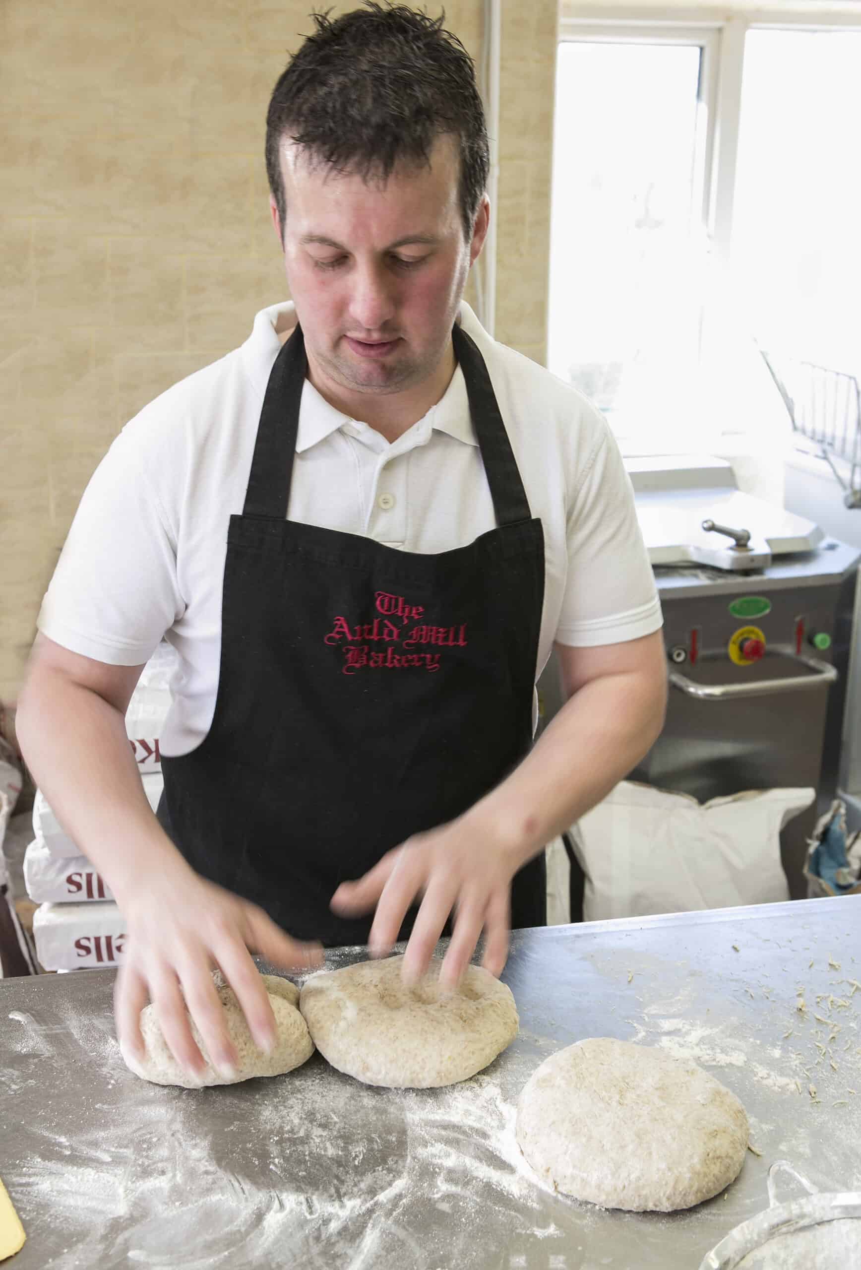 Freshly baked sourdough bread being shaped by a baker in the bakery.