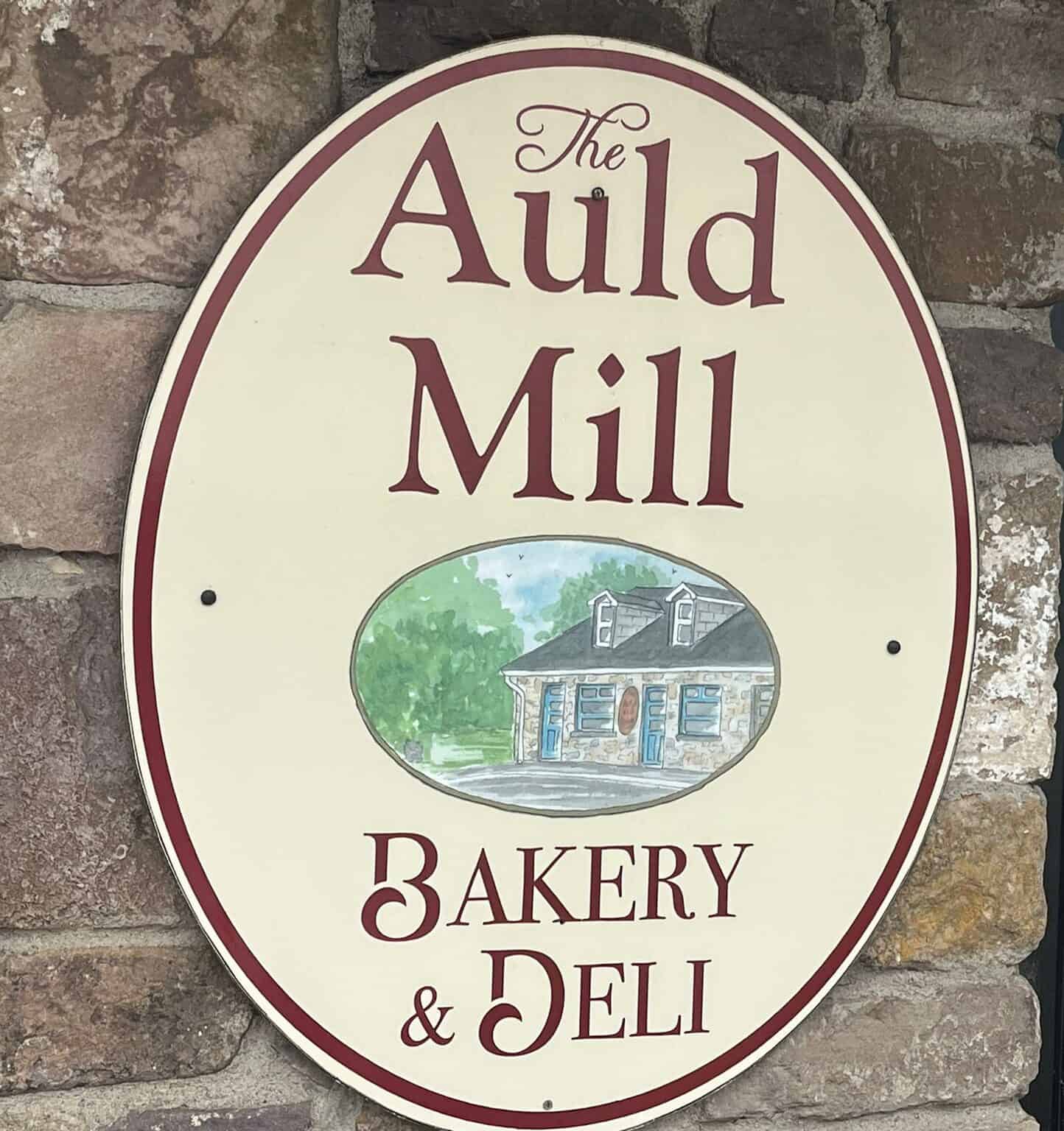 Auld Mill Bakery and Deli sign on stone wall, showcasing local bakery and deli services.