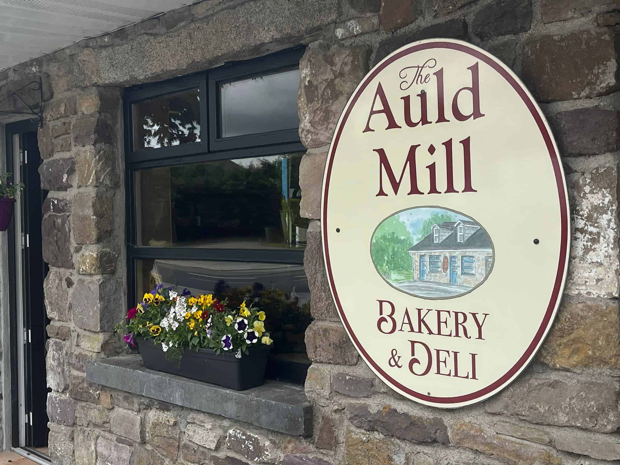 AULD MILL BAKERY & DELI sign on stone wall, showcasing the bakery's branding and inviting atmosphere.