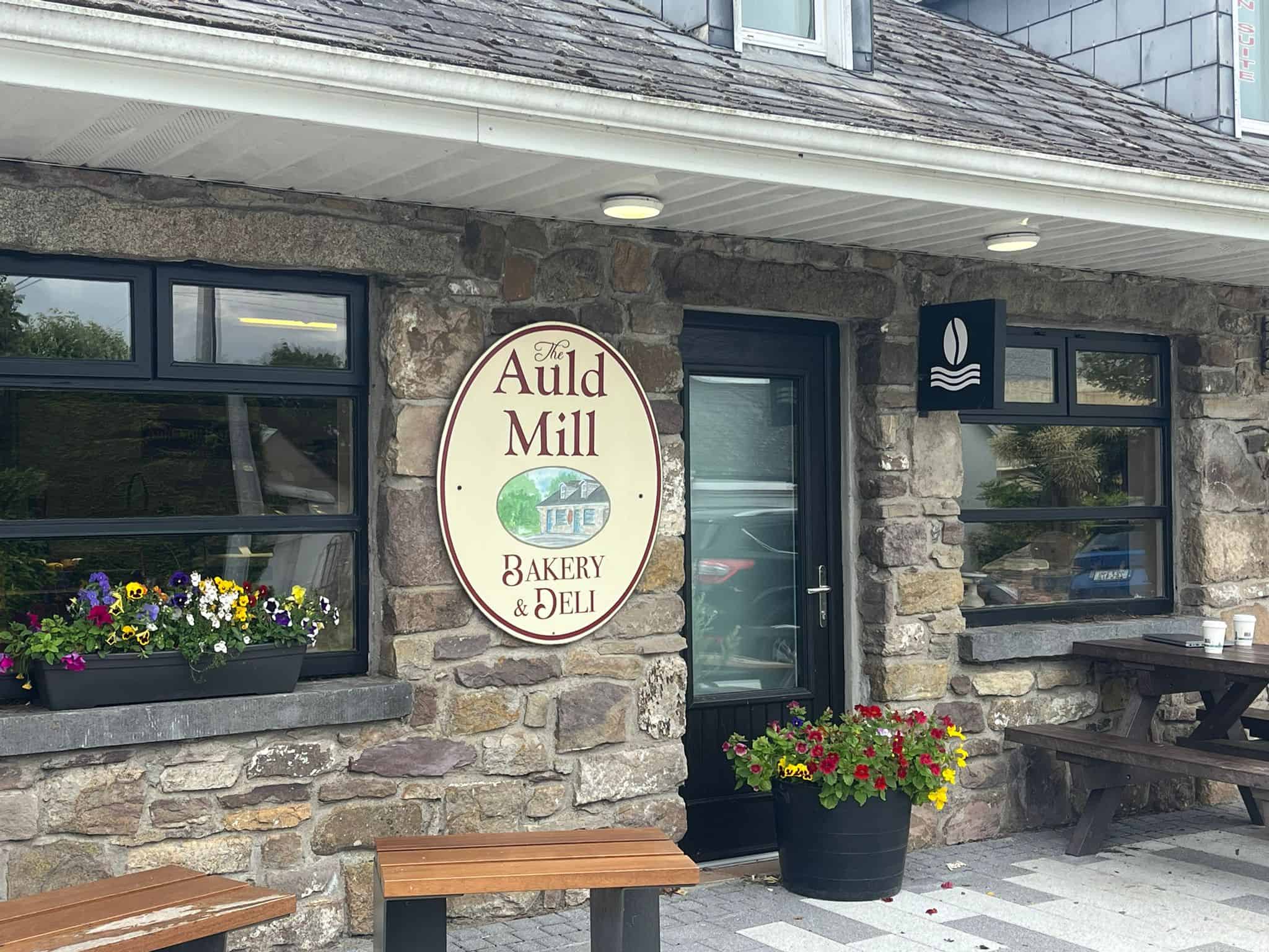 Exterior view of Auld Mill Bakery and Deli with stone facade and flower pots.